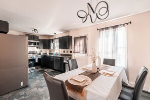 Cozinha moderna com armários escuros, uma área de jantar com mesa posta para quatro pessoas e um ventilador de teto.