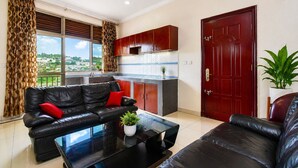 A living room with a black leather sofa, a coffee table, and a red door. - DV Appart Hotel (Kigali)