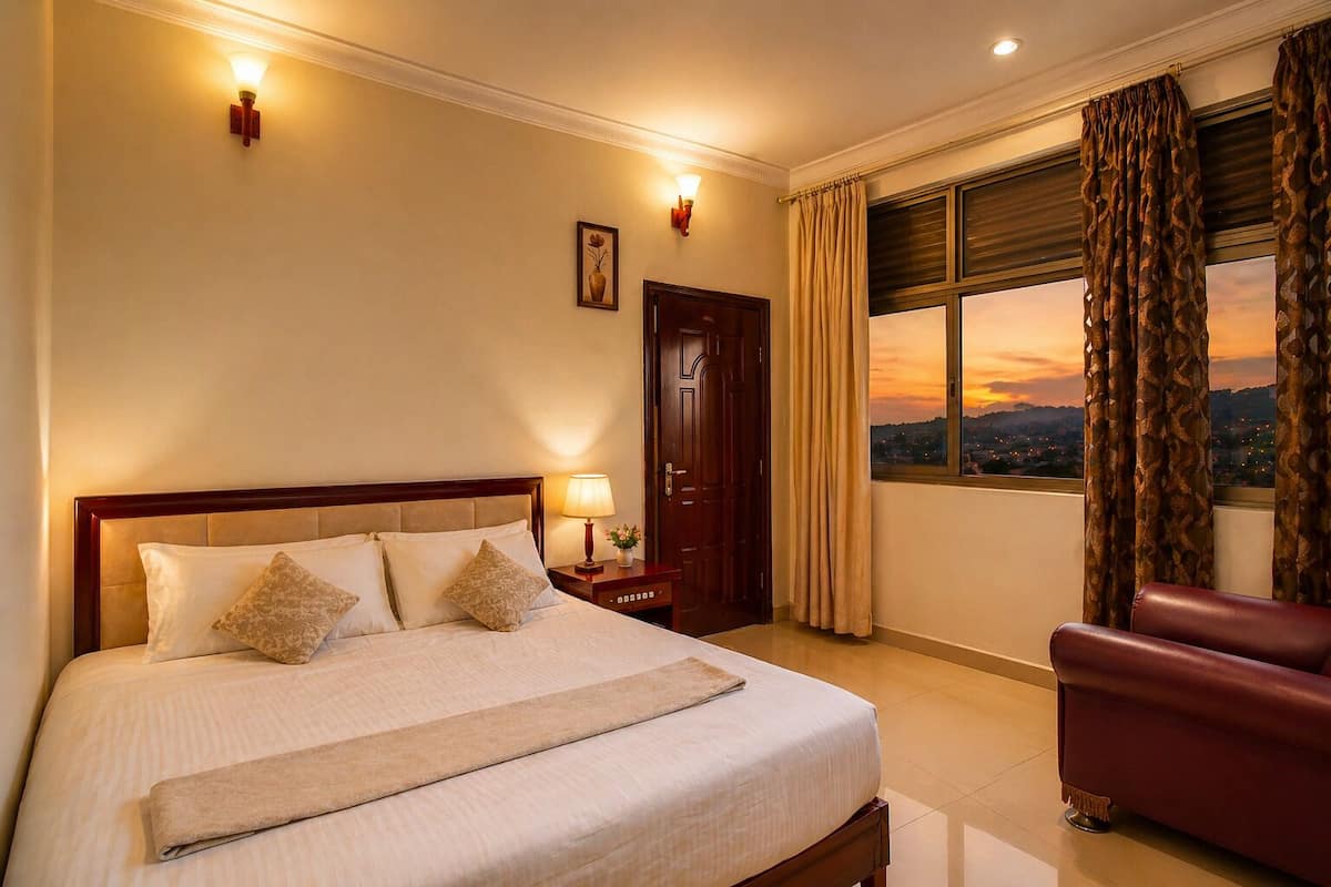 A hotel room with a bed, a nightstand with a lamp, a chair, a door, and a window with curtains.