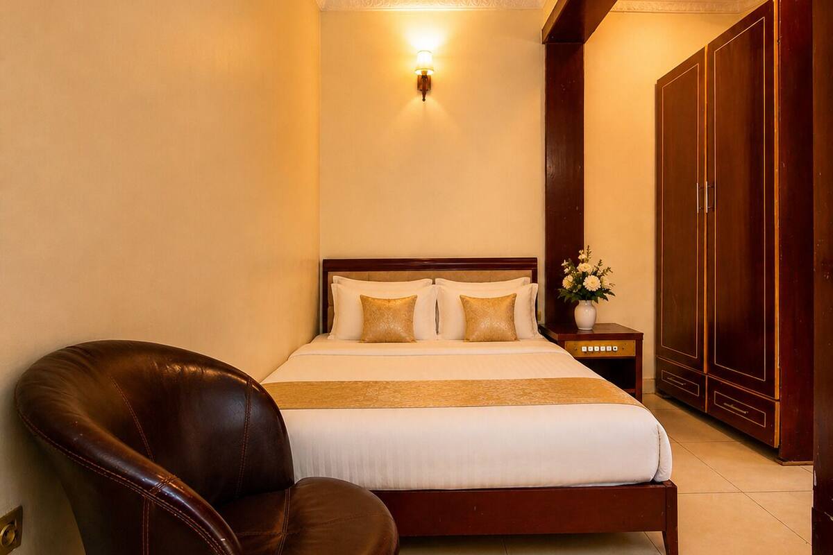 A hotel room with a bed, a nightstand with a lamp, a chair, and a wardrobe.
