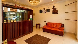 A reception area with a wooden counter, a chandelier, clocks, and a leather sofa. - DV Appart Hotel (Kigali)