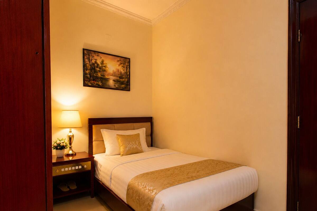 A hotel room with a bed, a nightstand, a lamp, and a painting on the wall.