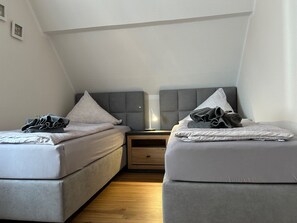 A twin room with two beds, a nightstand, a lamp, and a wooden floor. - Island star (Borkum)