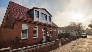 Ein zweistöckiges Ziegelhaus mit rotem Ziegeldach, weißen Fensterrahmen und einer kleinen Veranda.