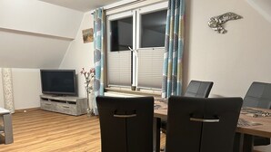 Ein Essbereich mit Tisch, Stühlen, einem Fernseher und einem Fenster mit Vorhängen.
