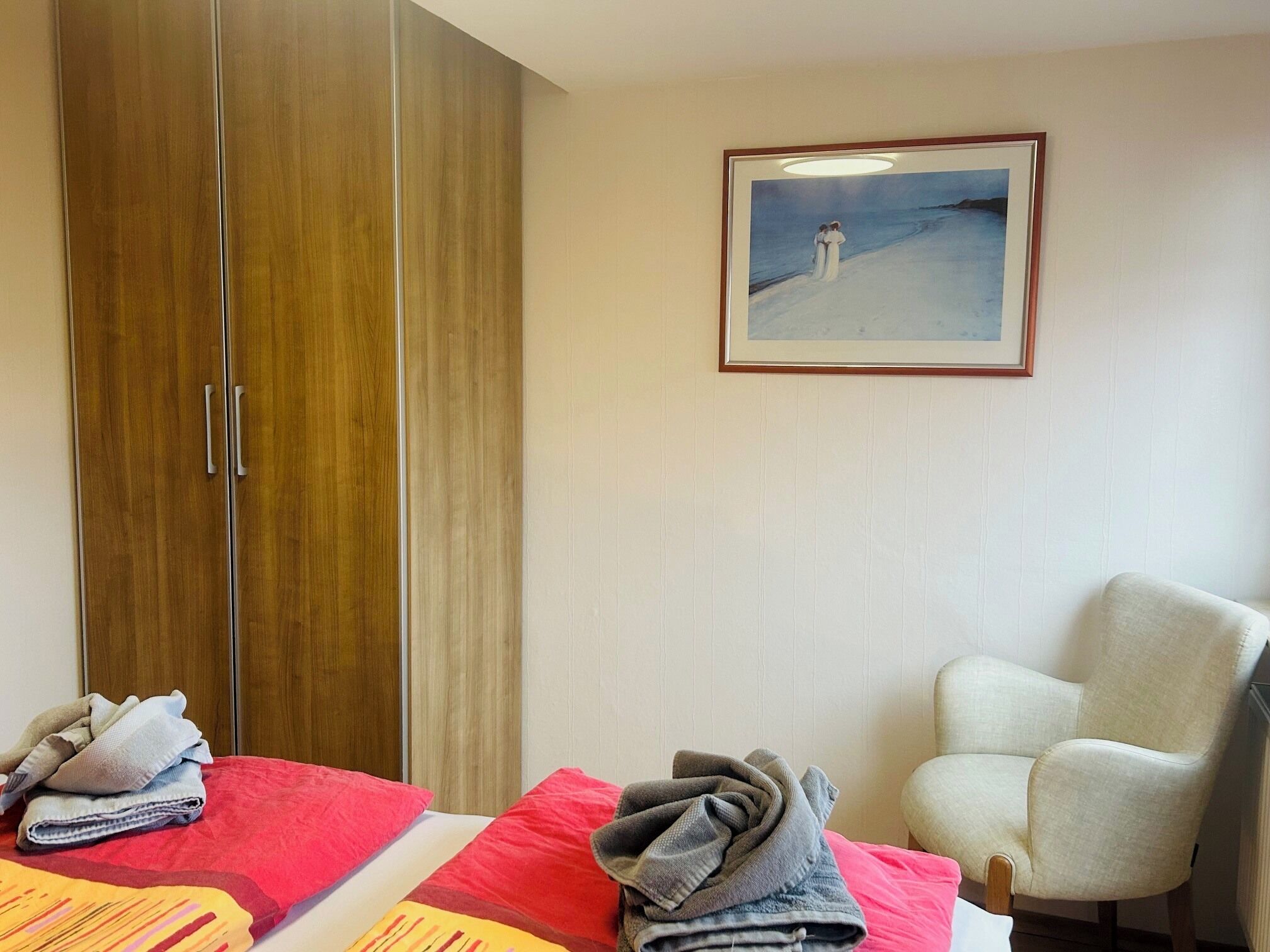Ein Hotelzimmer mit Bett, Sessel, Kleiderschrank und einem gerahmten Bild an der Wand.