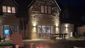 A stone house with a fire pit in the yard, outdoor seating, and a television visible inside.