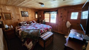 Une chambre dans une cabane en bois, avec un grand lit, une commode, un bureau et une fenêtre avec des stores.