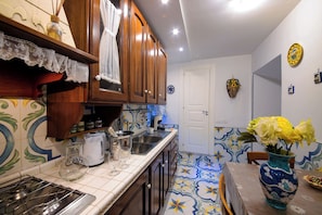 A kitchen with wooden cabinets, a tiled backsplash, a stove, and a vase with flowers. - Comfortable apartment in the heart of Naples (Napoli)