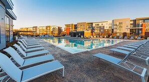 Un área de piscina en la azotea con sillones de descanso y vistas a edificios de varios pisos.