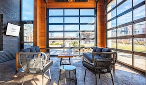 Un espacio interior amplio con mobiliario de mimbre, ventanas grandes y vistas a la ciudad.