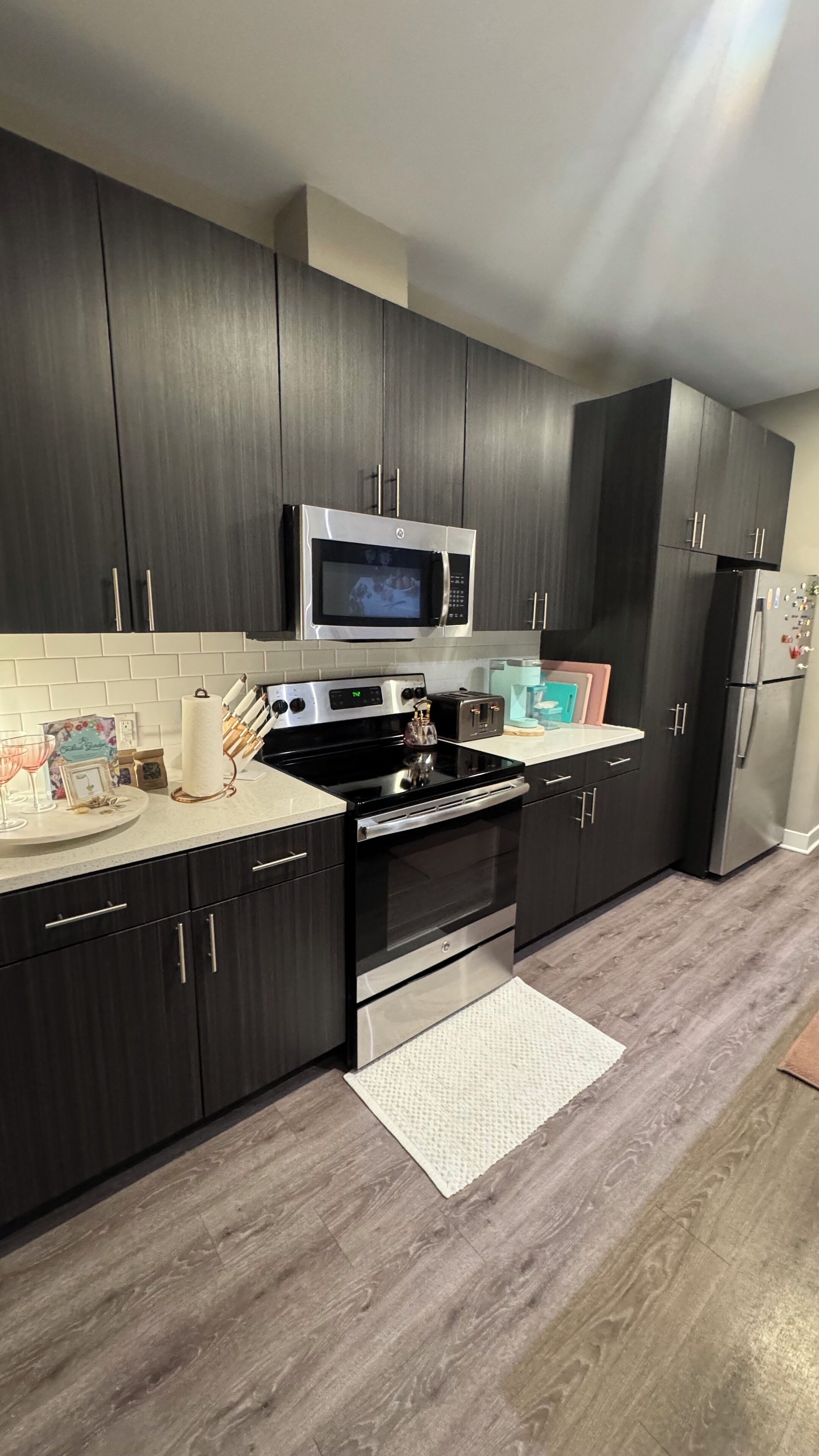 A modern kitchen with dark cabinetry, a stainless steel microwave, a gas stove, and a built-in oven.