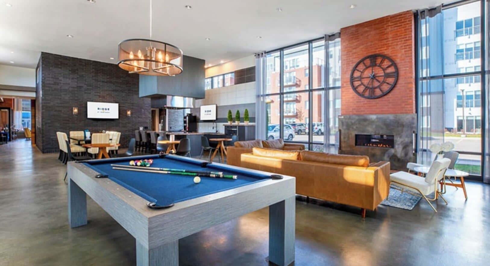 Un espace piscine intérieur moderne, doté d’une table de billard, de coins salon et d’une cheminée.