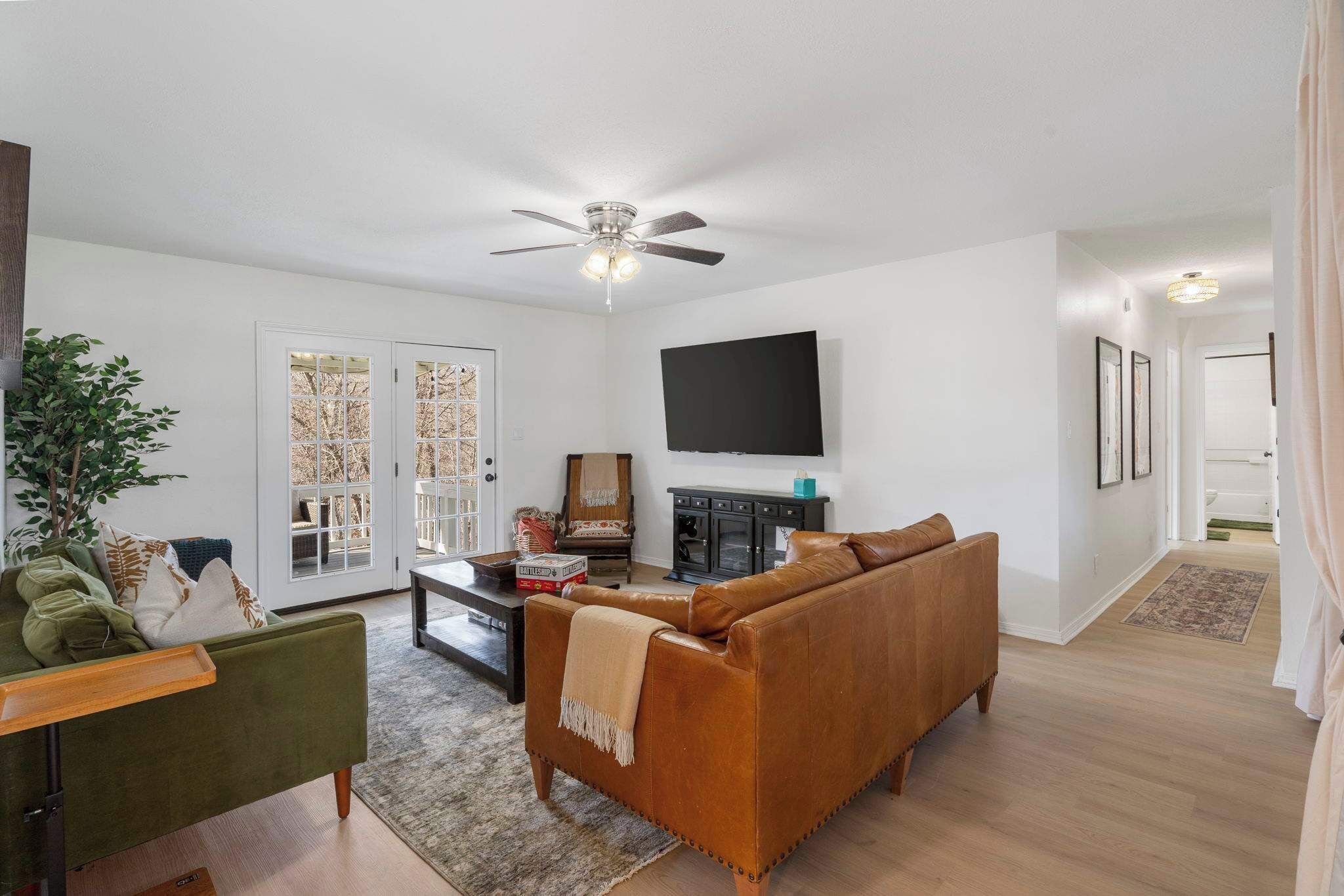 A living room with a brown leather sofa, a green armchair, a coffee table, and a ceiling fan.