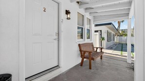 Eine überdachte Veranda mit einer Bank, einer weißen Tür mit Hausnummer und Blick auf die Straße.