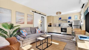 A modern living room with a grey sofa, a coffee table, and a dining area with a table and chairs. - Covare Suite 4 (St. Pete Beach)