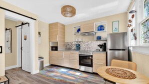 A modern kitchen with wooden cabinets, a stainless steel refrigerator, and a dining area with a table and chair. - Covare Suite 4 (St. Pete Beach)