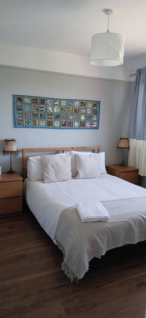 A neatly made bed with white linens, a wooden headboard, and a white throw blanket. There is a colorful tapestry on the wall above the bed, and a hanging light fixture above it. - Cozy 2-bedroom Apartment in Central London (London)