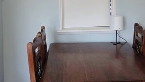 Una sala da pranzo con un tavolo e sedie in legno, una finestra con persiane e una lampada da tavolo.