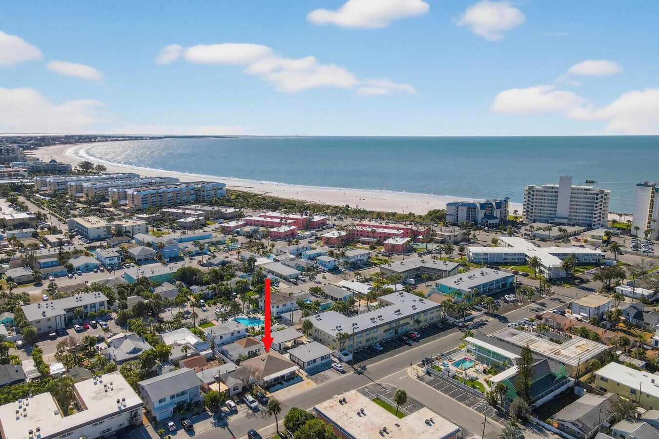 Una vista aerea di una località balneare con spiaggia, hotel e una grande freccia rossa che indica un edificio specifico.