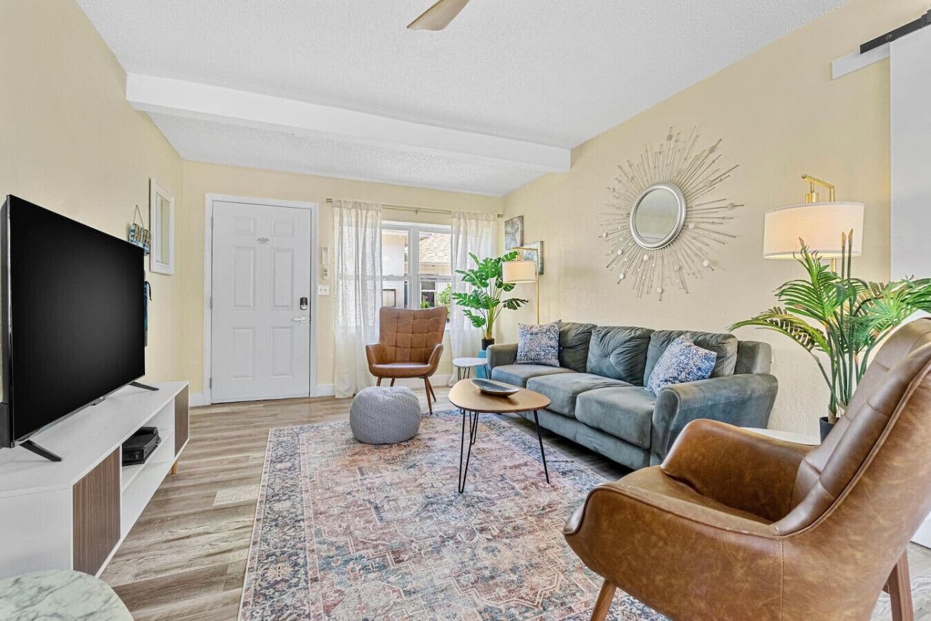 Un salon comprenant un téléviseur à écran plat, un canapé, un fauteuil en cuir marron, une table basse et un tapis à motifs.
