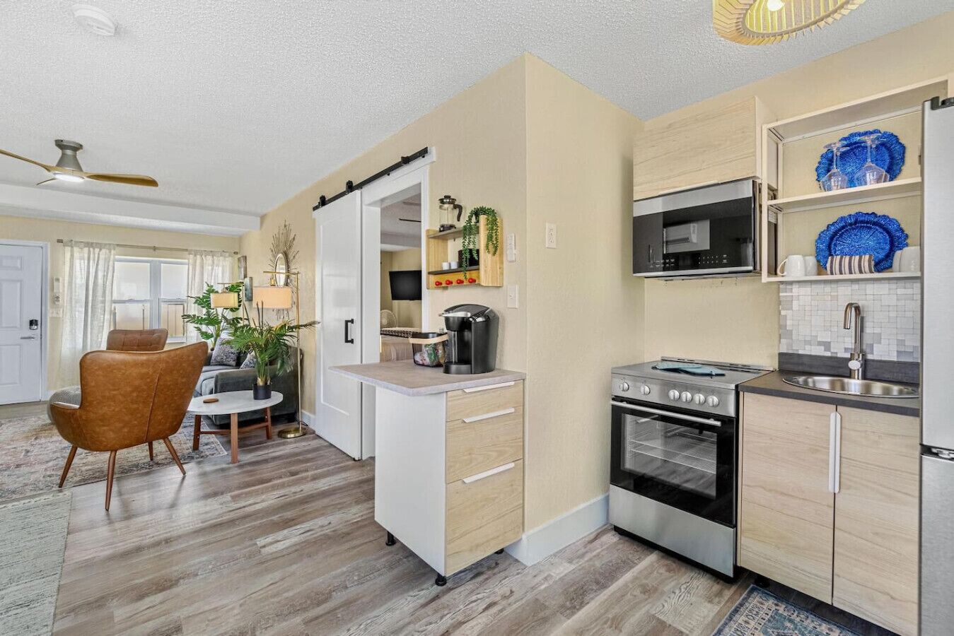 A compact kitchen with a microwave, oven, and sink, a dining area with a chair and table, and a ceiling fan.