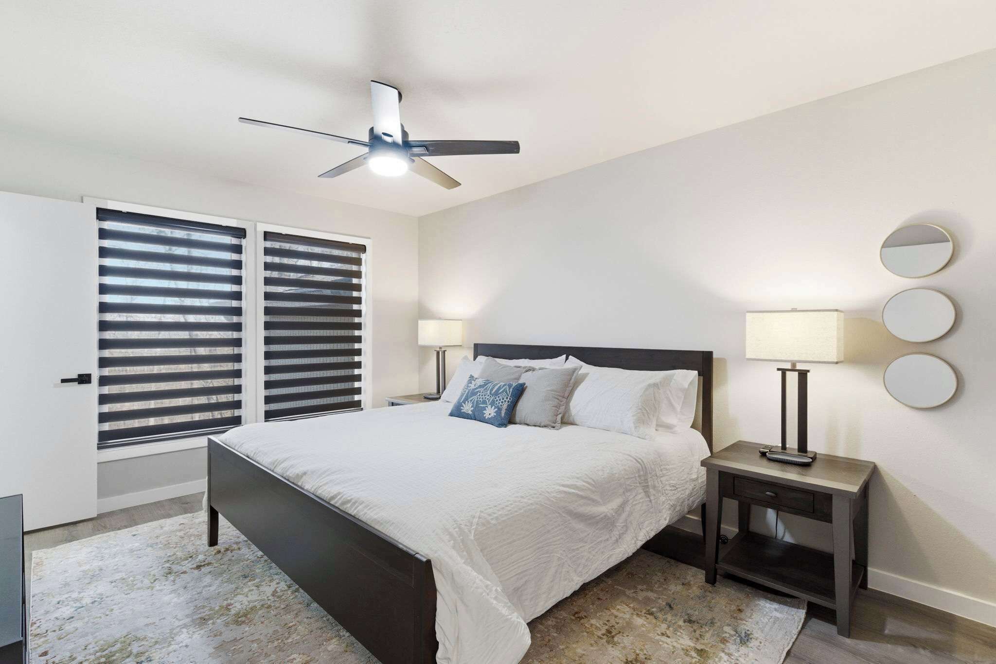 Un dormitorio con cama, mesitas de noche, ventilador de techo y ventana con persianas.