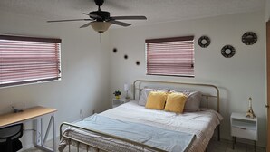 Une chambre à coucher comprenant un lit, des tables de chevet, un bureau et un ventilateur de plafond.