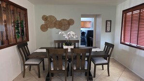 Un coin repas comprenant une table et des chaises, un élément décoratif mural et une fenêtre avec des stores.