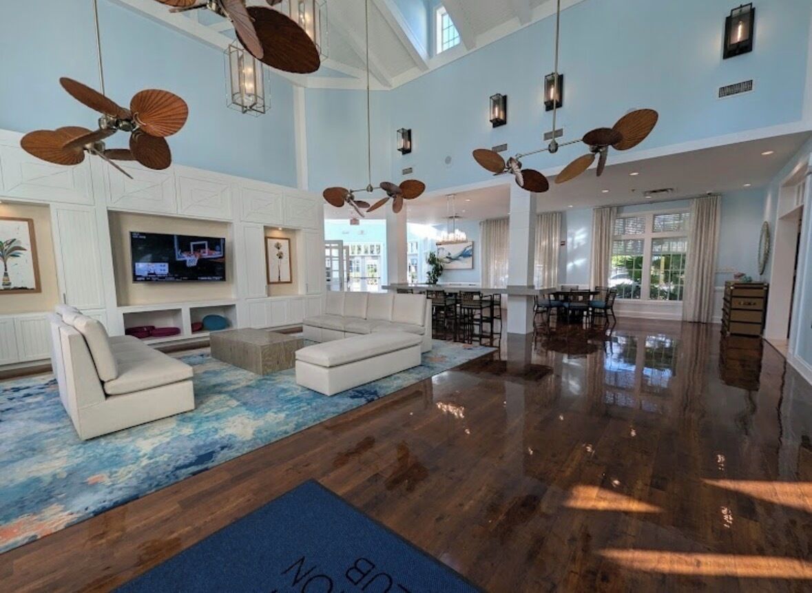 A spacious living area with a large sofa, a TV, ceiling fans, and a wooden floor.