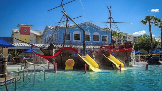 Een waterpark met een glijbaan met piratenthema en een gebouw met een blauwe gevel op de achtergrond.