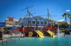 Een waterpark met een glijbaan met piratenthema en een gebouw met een blauwe gevel op de achtergrond.