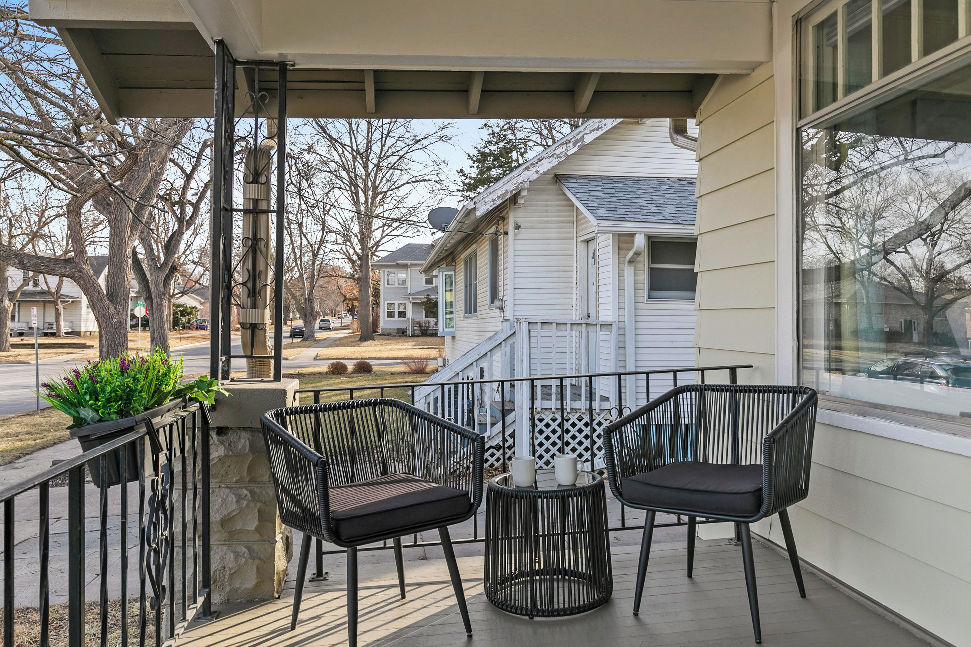 Un balcon avec deux fauteuils en osier noir et une petite table ronde, donnant sur une rue résidentielle.