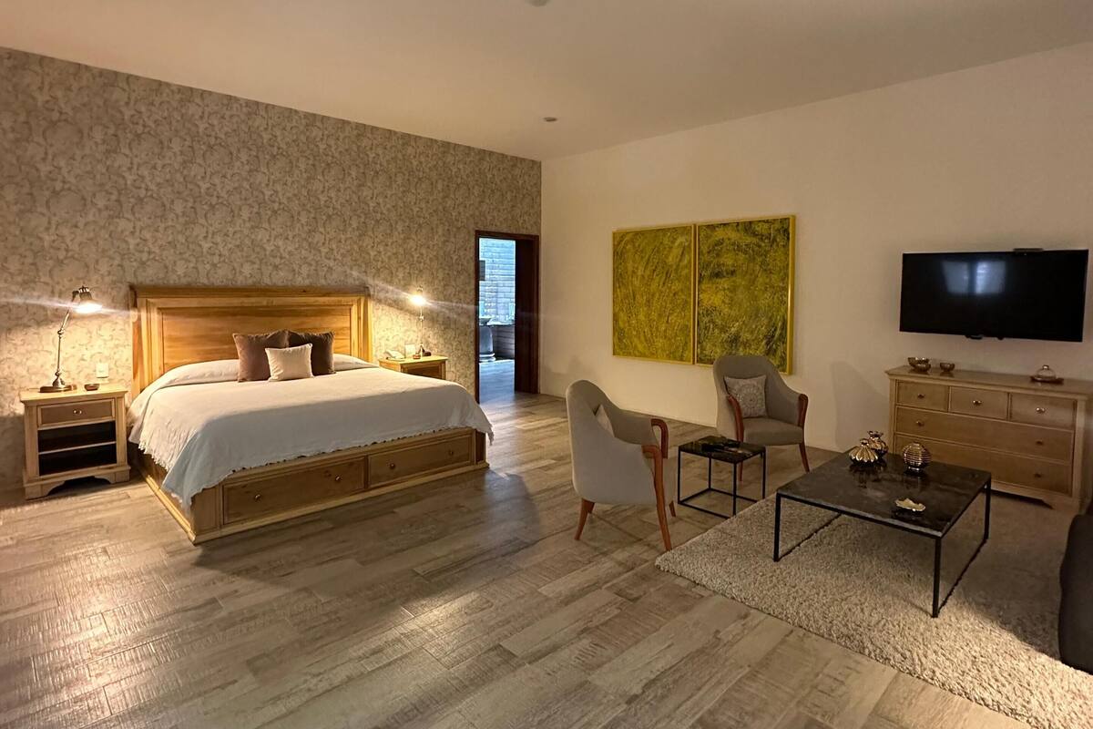 Een moderne slaapkamer met een groot bed, nachtkastjes, een flatscreen-tv, een salontafel en een zithoek.