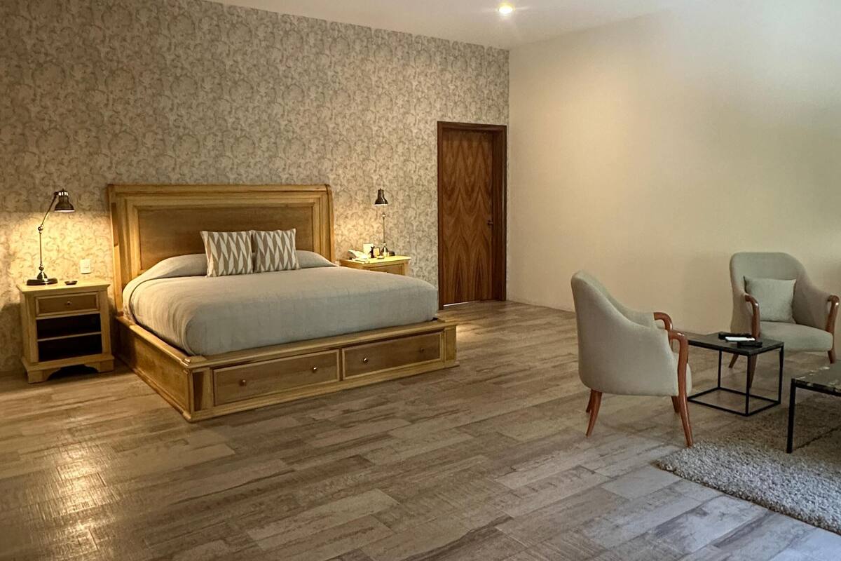 Een slaapkamer met een houten bed, twee nachtkastjes, een stoel en een deur.