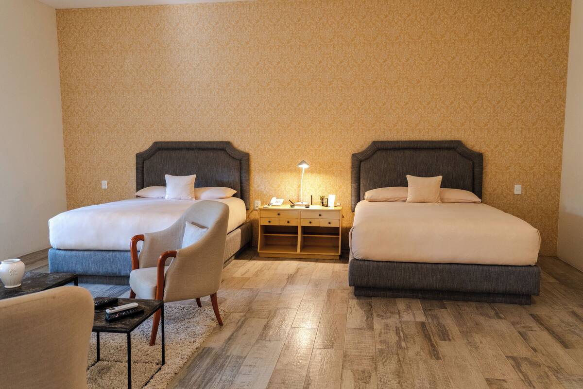 Een hotelkamer met twee bedden, een nachtkastje, een lamp, een stoel en een klein tafeltje.