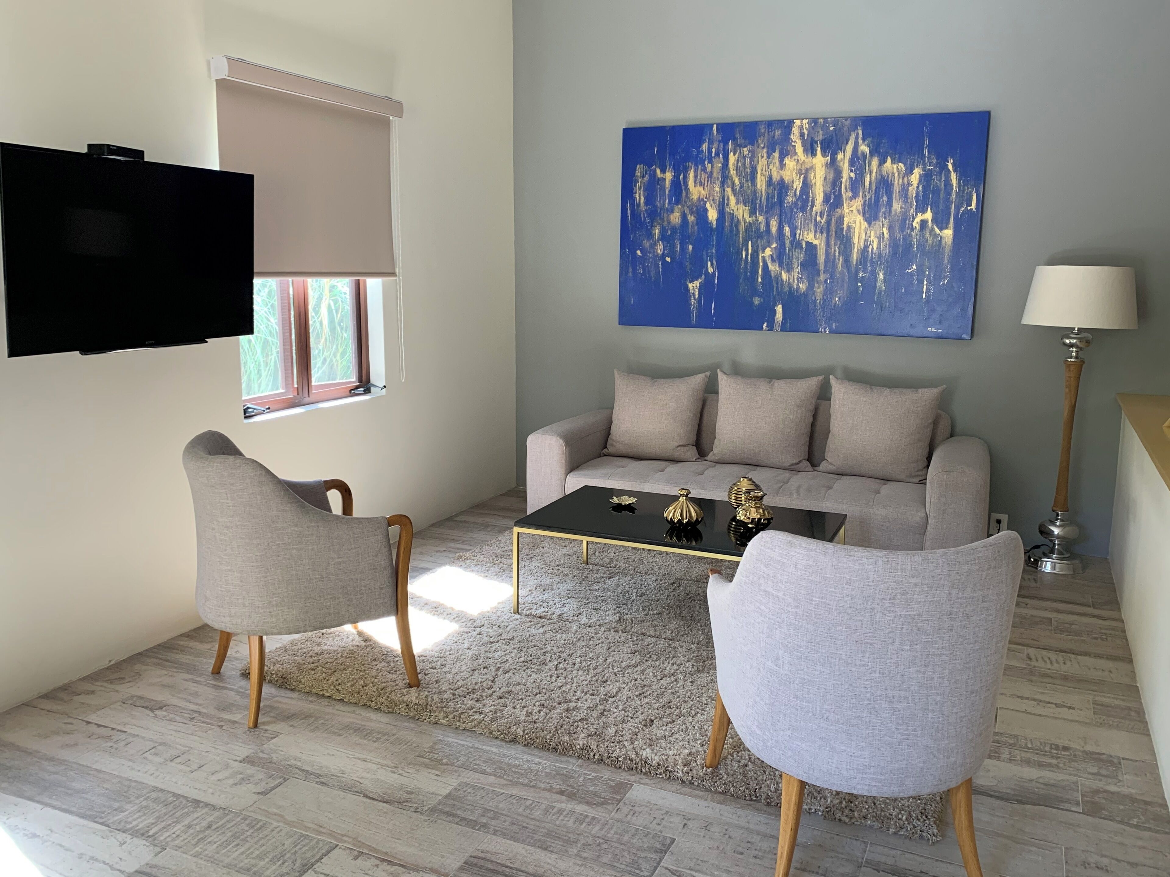 Un salon moderne avec un canapé, deux fauteuils, une table basse, un téléviseur et un tableau accroché au mur.