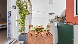 Eine kleine Terrasse mit Tisch und Stühlen, umgeben von weißen Mauern und einem grünen Zaun.