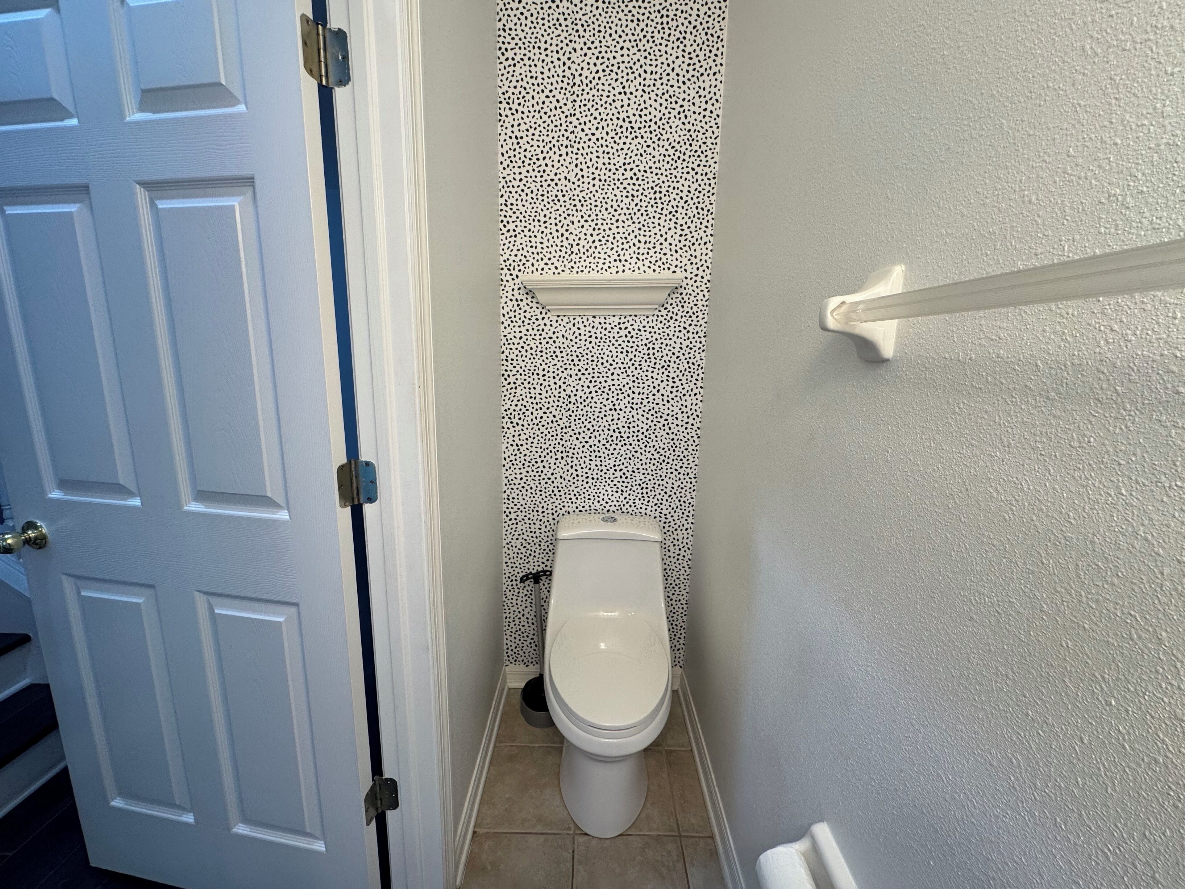 Een badkamer met een toilet, een witte deur en een behang met patroon.