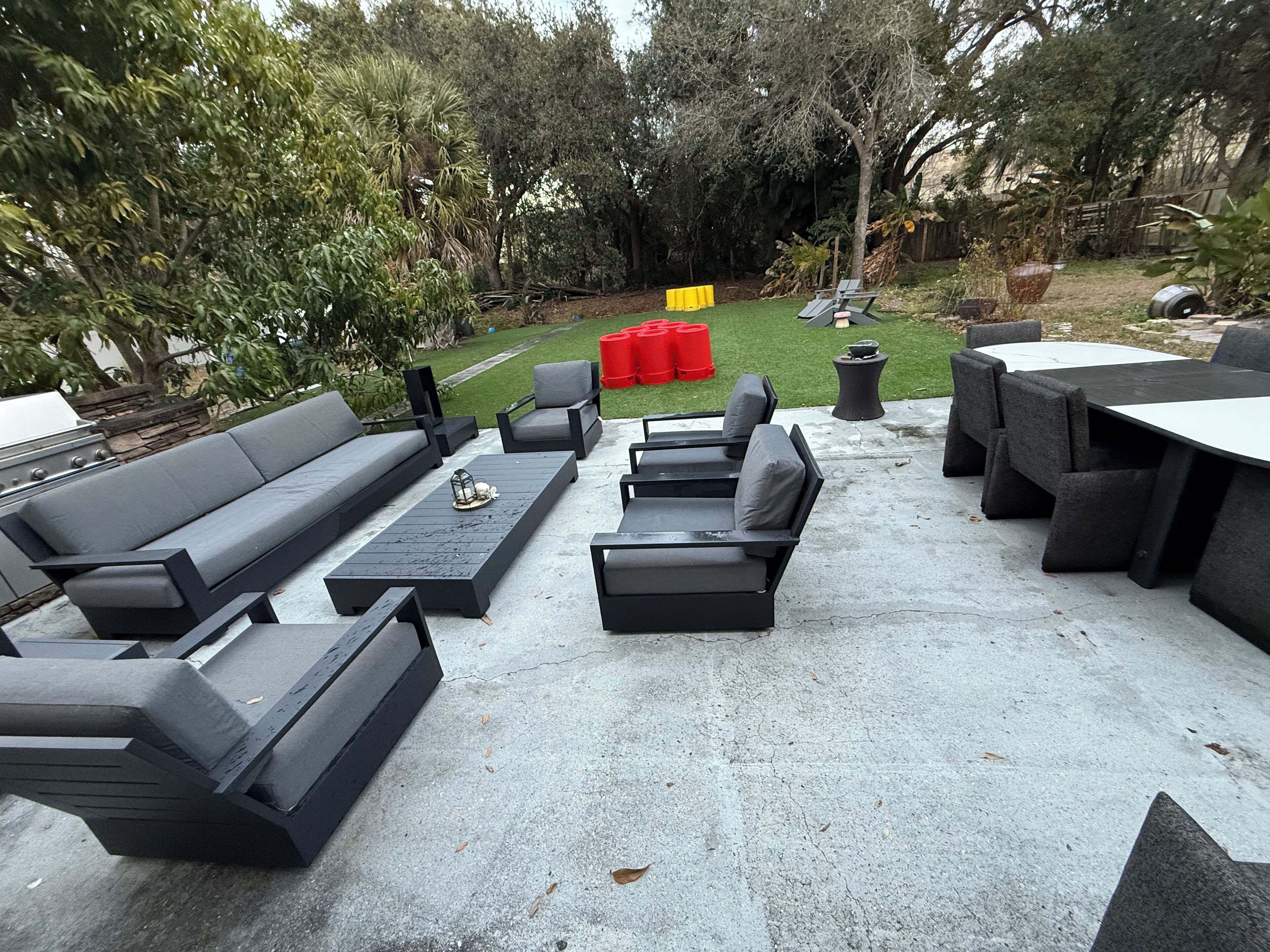 Un patio exterior con un sofá negro, dos sillones reclinables negros, una mesa redonda y un pequeño hogar para fuego.