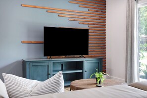 Ein modernes Zimmer mit einem Flachbildfernseher auf einer blauen Kommode, einem runden Holztisch mit einer Pflanze und einem weißen Sofa.