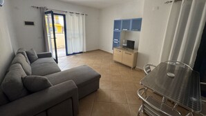 Ein Wohnzimmer mit einer Couch, einem Esstisch und einer Küchenzeile mit Schränken und einem Fernseher.