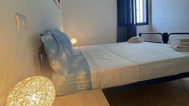 Ein Schlafzimmer mit einem Bett, einer Nachttischlampe, einem Fenster mit Vorhängen und einem an der Wand befestigten Lichtschalter.