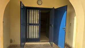 Ein offenes, blaues Tor führt zu einem Gebäude mit Fliesenboden und einem Rundfenster über der Tür.