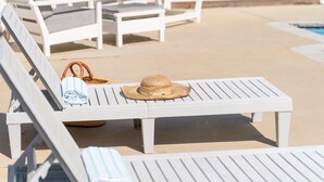 A poolside area with white lounge chairs, a table, and a straw hat. - Sunny Bungalow Retreat w/Pool + 6 Person Golf Cart Included (Emerald Isle)