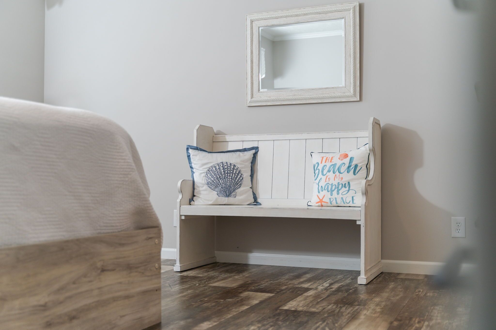 A white bench with a mirror above it and two pillows with text.