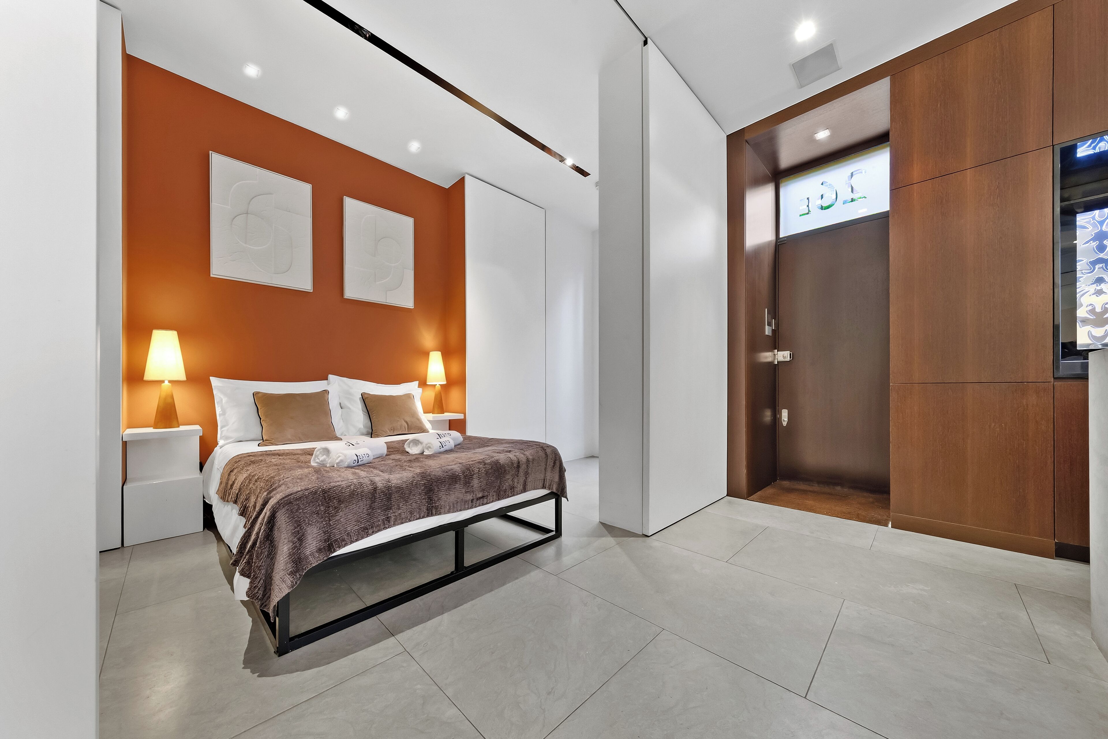 A modern hotel room with a bed, nightstands, and a wardrobe.