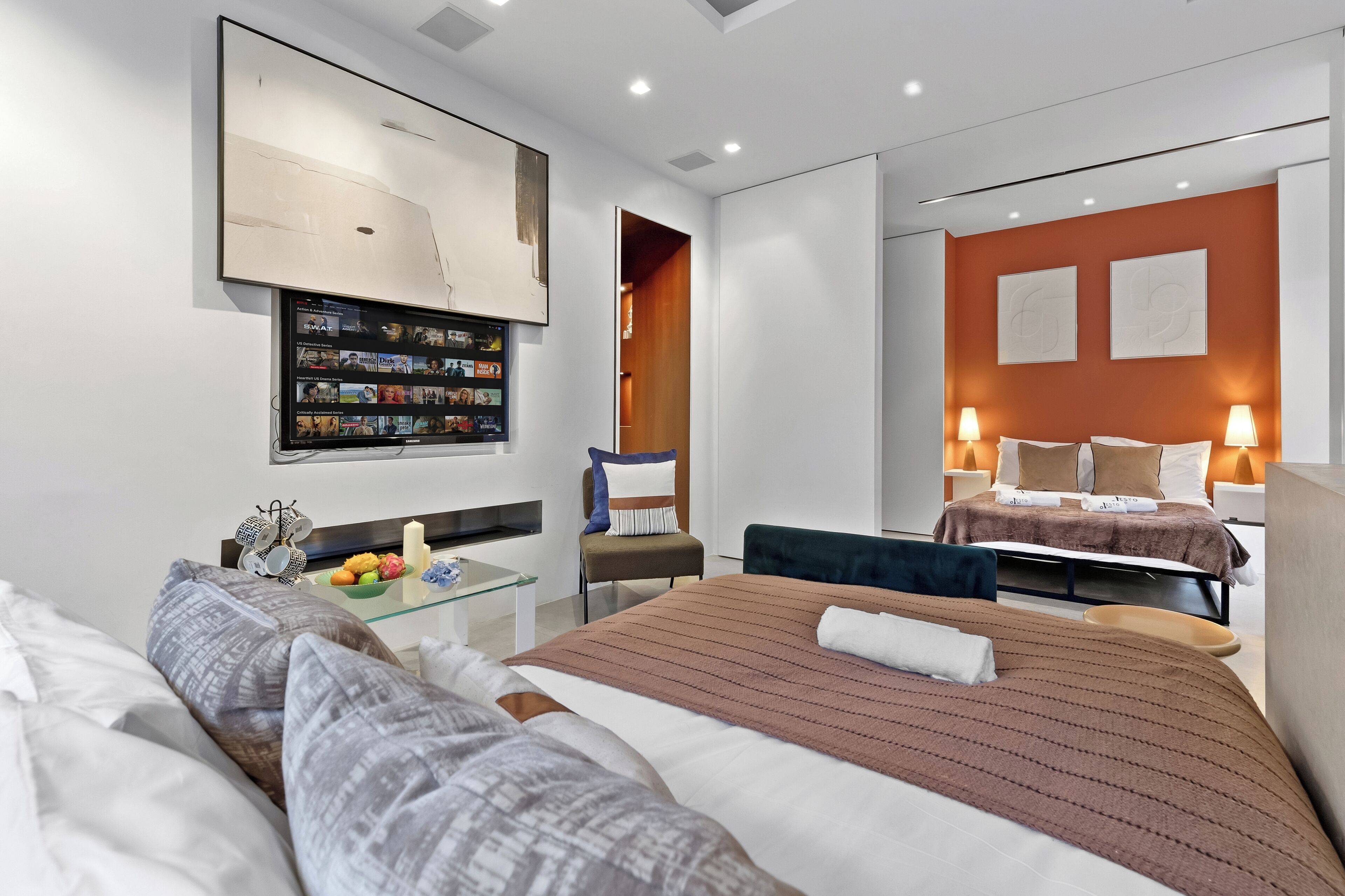 Une chambre d’hôtel moderne dotée d’un grand lit, d’un bureau avec un ordinateur, d’une table basse en verre et d’un téléviseur fixé au mur.