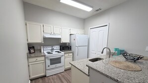 A compact kitchen with white cabinets, a stove, microwave, and refrigerator. - Cozy Beachy Riverwalk Condo – Close to Downtown & Beaches (Pensacola)