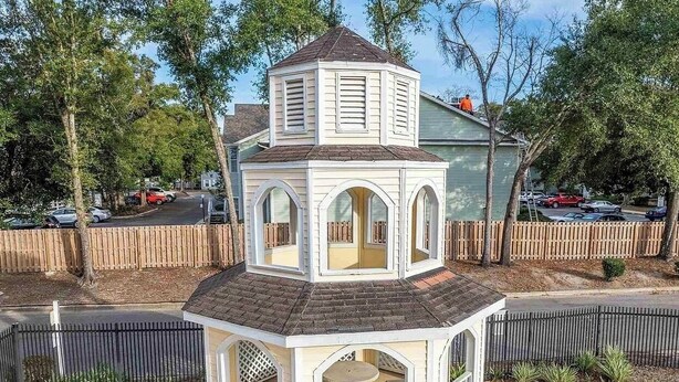 A gazebo-style structure with a central table and benches, surrounded by a fence and trees. - Cozy Beachy Riverwalk Condo – Close to Downtown & Beaches (Pensacola)